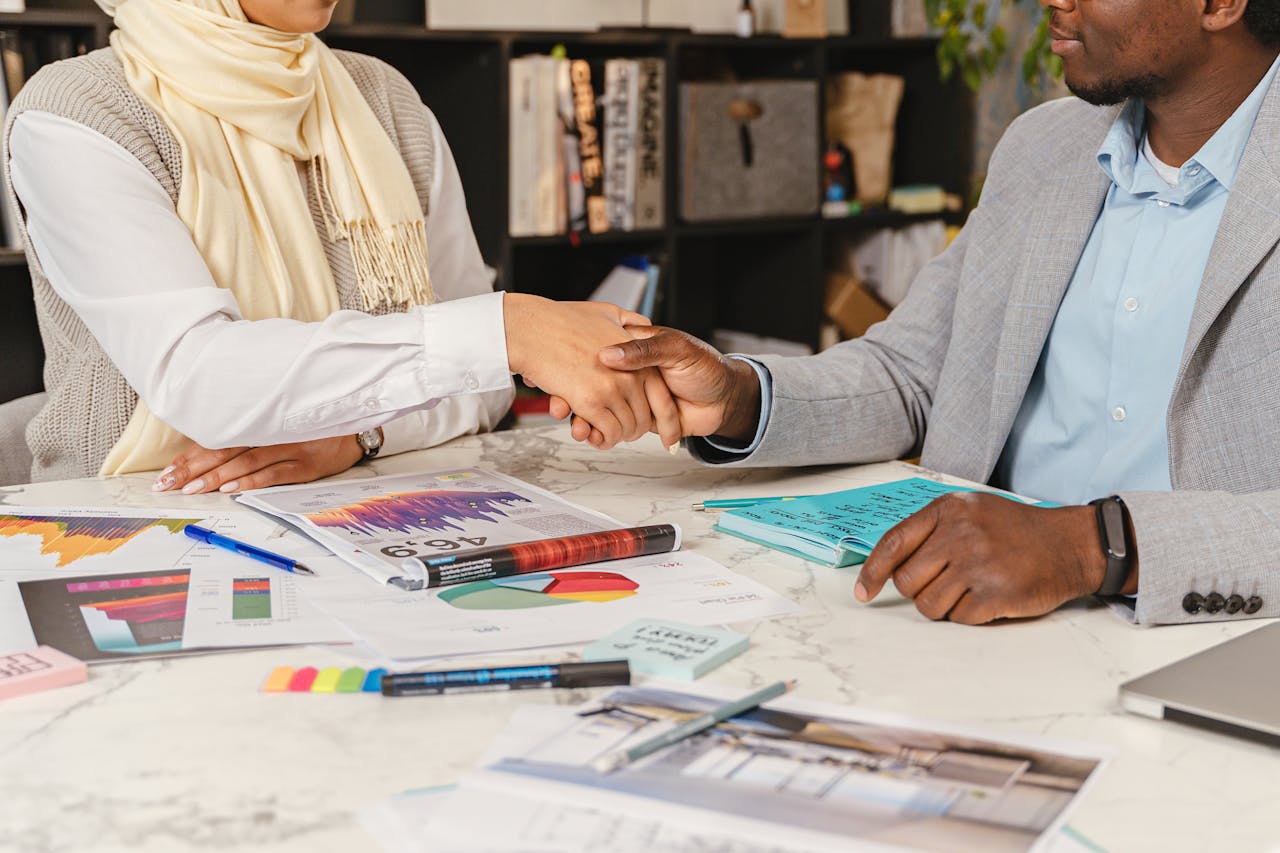Mastering the First Impression: Your intriguing post title goes here Two business professionals shaking hands over financial documents in an office setting.